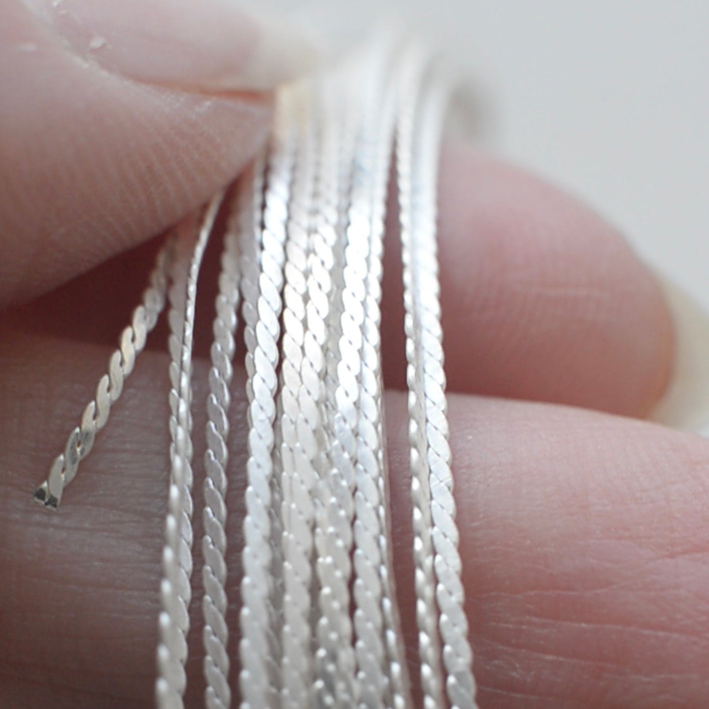 Close-up of hands holding silver braided wire against a white background