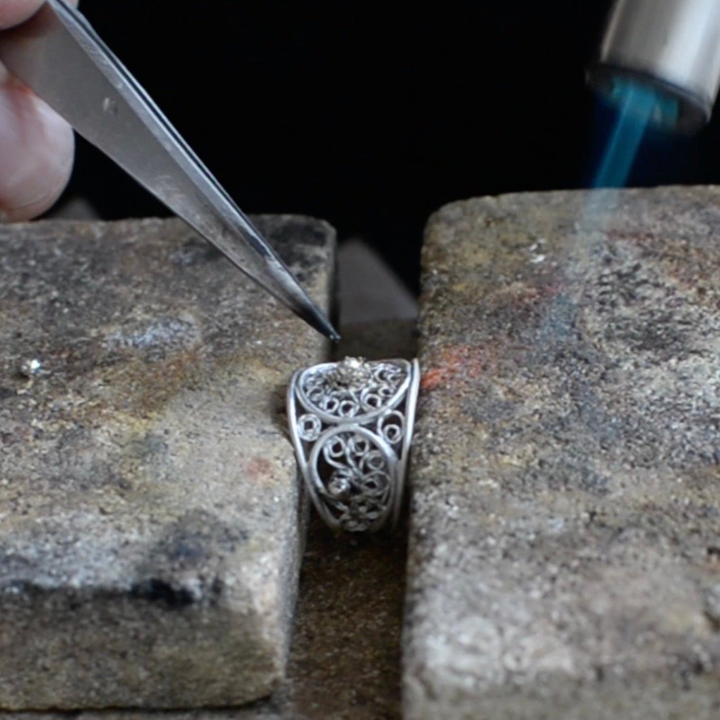 Silver filigree ring being worked on with tools on a stone surface