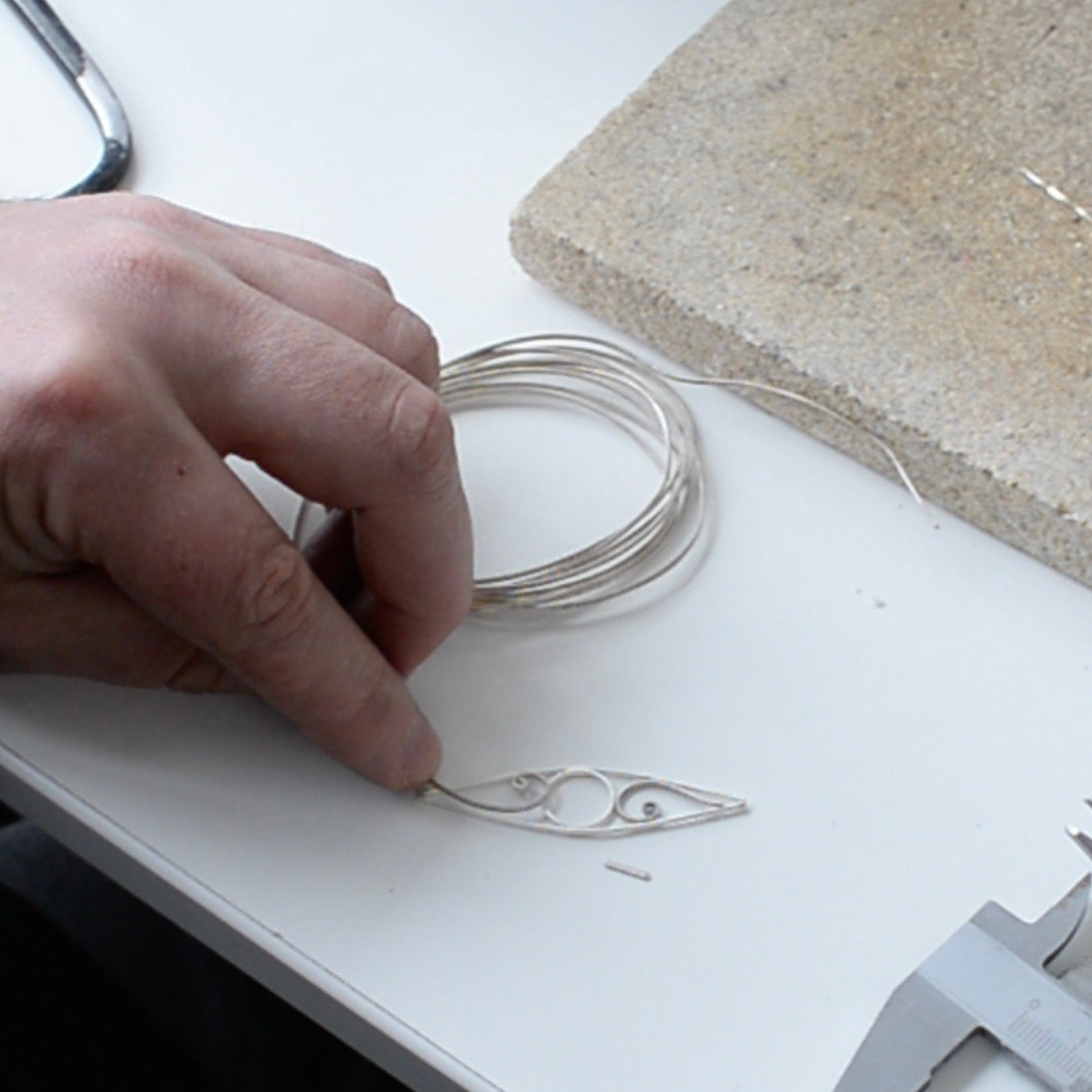 Hand holding wire near a piece of paper with a design on a white surface.