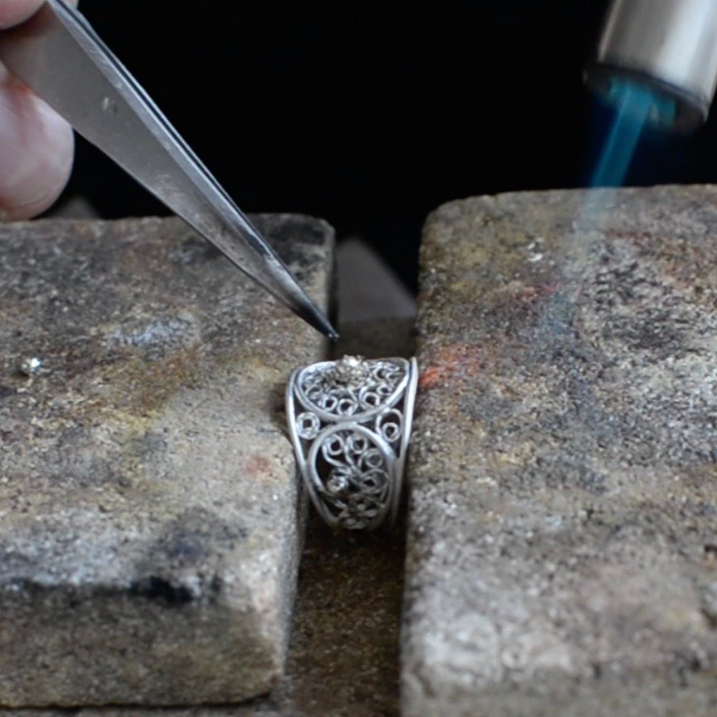 Silver filigree ring being worked on with tools on a stone surface